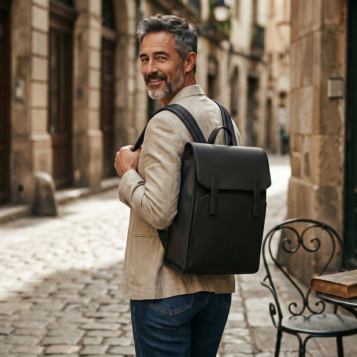 Homme portant un sac à dos Le Voyage Prestige noir en cuir PU et Oxford dans une rue pavée européenne