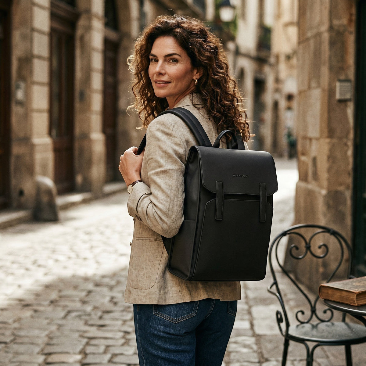Femme portant un sac à dos noir Le Voyage Prestige en cuir synthétique, style business élégant dans une rue pavée.