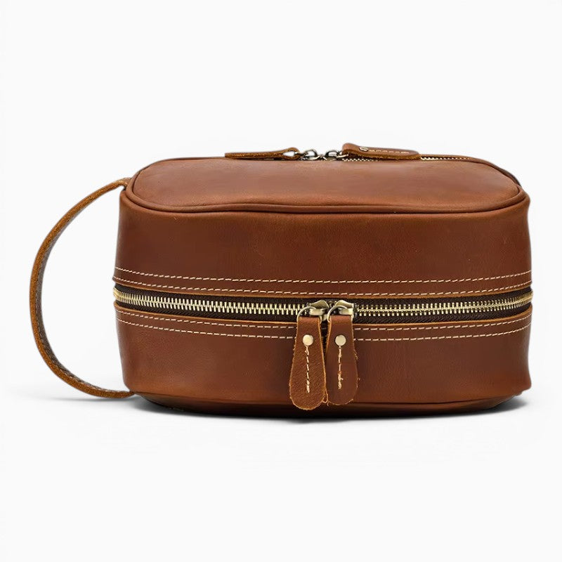 Le Voyage Prestige Sac de voyage compact en cuir marron avec double fermeture éclair et poignée latérale.