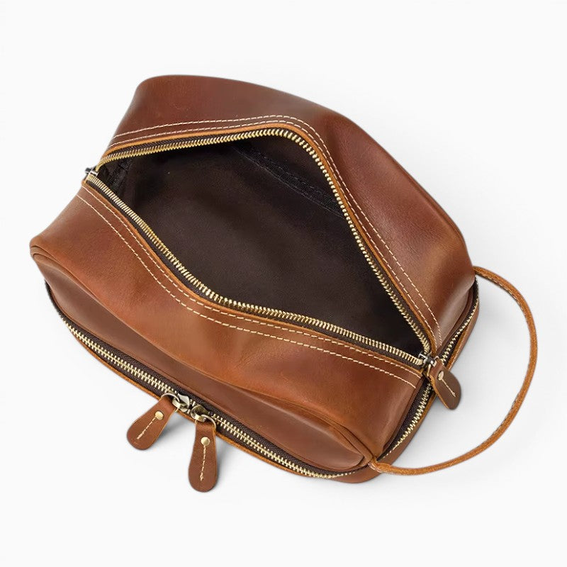 Le Voyage Prestige Sac de voyage compact en cuir marron avec fermeture éclair et coutures contrastées, idéal pour les articles de toilette.