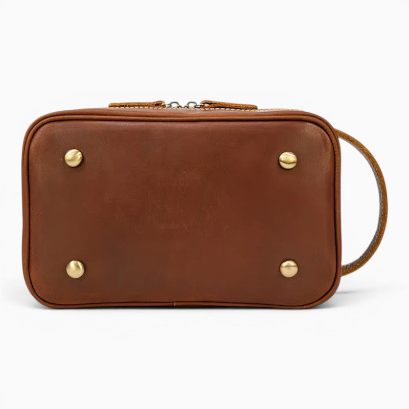 Le Voyage Prestige Sac de voyage compact en cuir marron avec fermeture éclair et pieds métalliques, idéal pour le maquillage ou les articles de toilette.