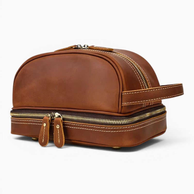 Le Voyage Prestige sac de voyage compact en cuir marron avec double fermeture éclair et poignée latérale.
